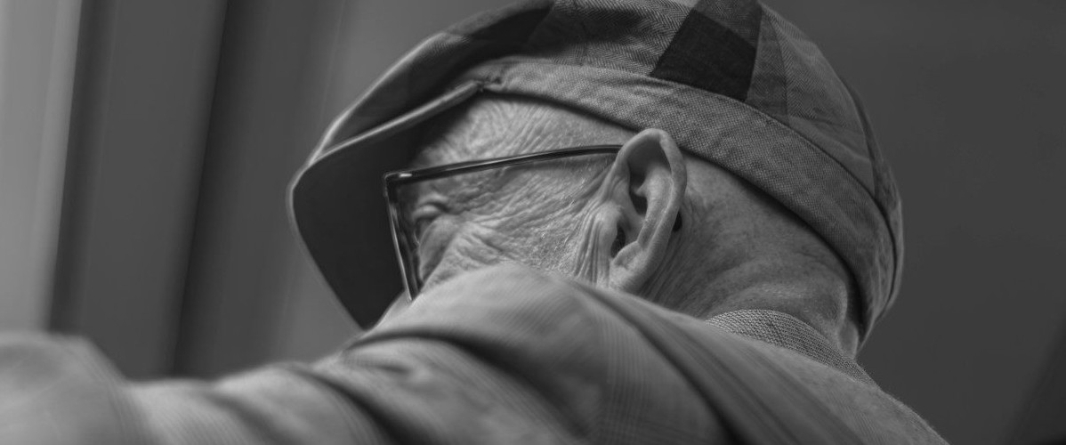 An elderly man wears a hat and glasses.