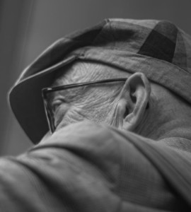 An elderly man wears a hat and glasses.