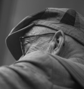 An elderly man wears a hat and glasses.