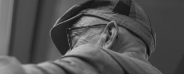An elderly man wears a hat and glasses.