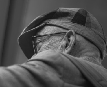 An elderly man wears a hat and glasses.