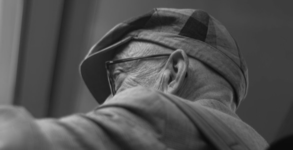An elderly man wears a hat and glasses.