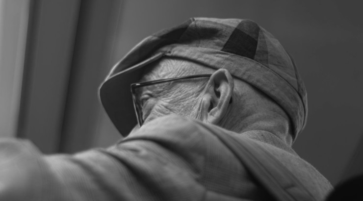 An elderly man wears a hat and glasses.
