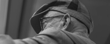 An elderly man wears a hat and glasses.