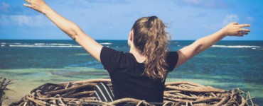 woman in black shirt sitting on brown wooden log near body of water during daytime