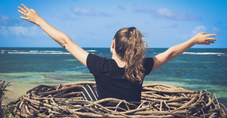 woman in black shirt sitting on brown wooden log near body of water during daytime