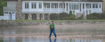 Serene scene of a man fishing in front of a grand lakeside mansion.