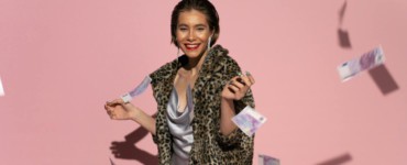 Stylish woman in fur coat with flying euro notes and pink background. Bright, fashionable, and confident.
