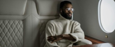 A stylish man in a turtleneck relaxes inside a private jet, embodying luxury travel.