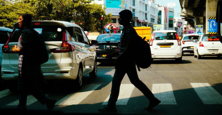 People crossing a busy city street with cars.
